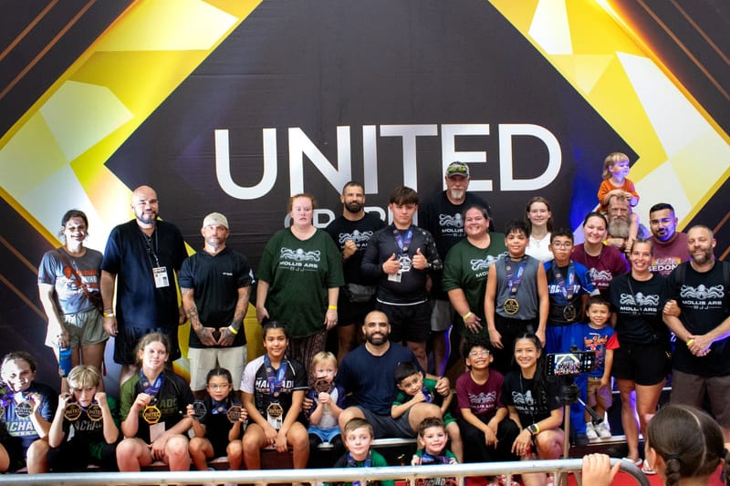 A large group of athletes, parents and coaches in Mollis Ars team shirts pose together at a tournament.