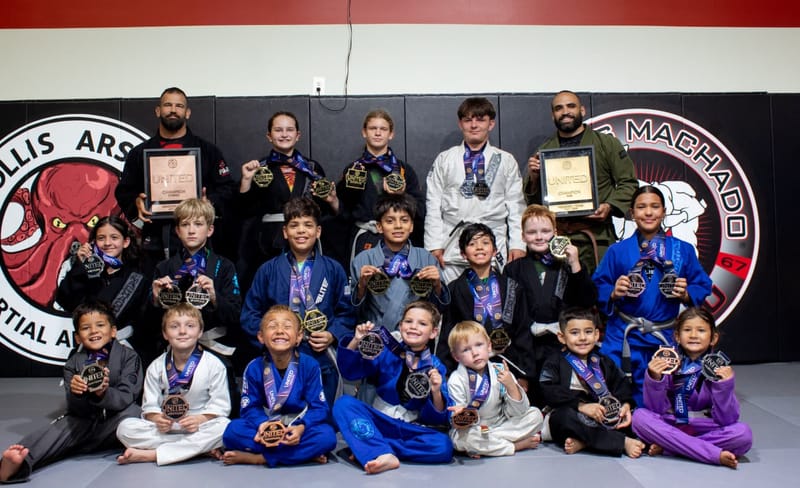 The Mollis Ars BJJ kids competition team poses with two coaches, holding medals and champion plaques.