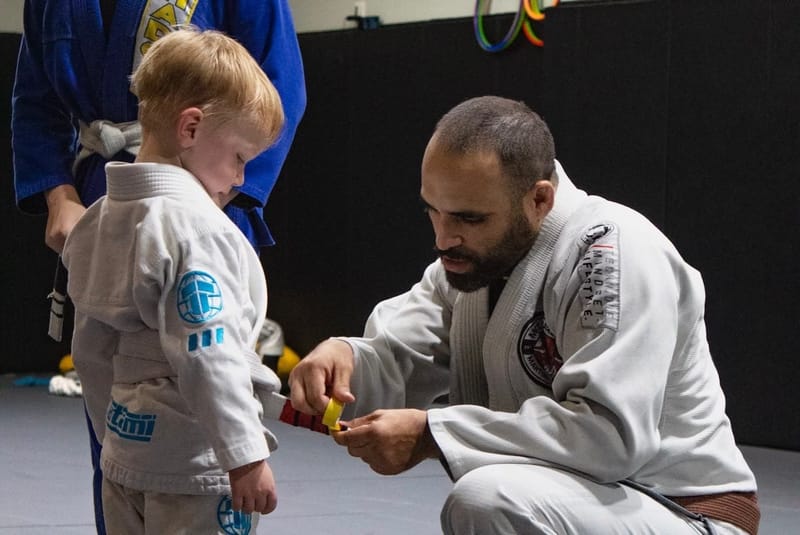 An instructor tying a striped belt on a young student