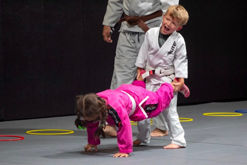 Kids laughing through a wheelbarrow push-up drill