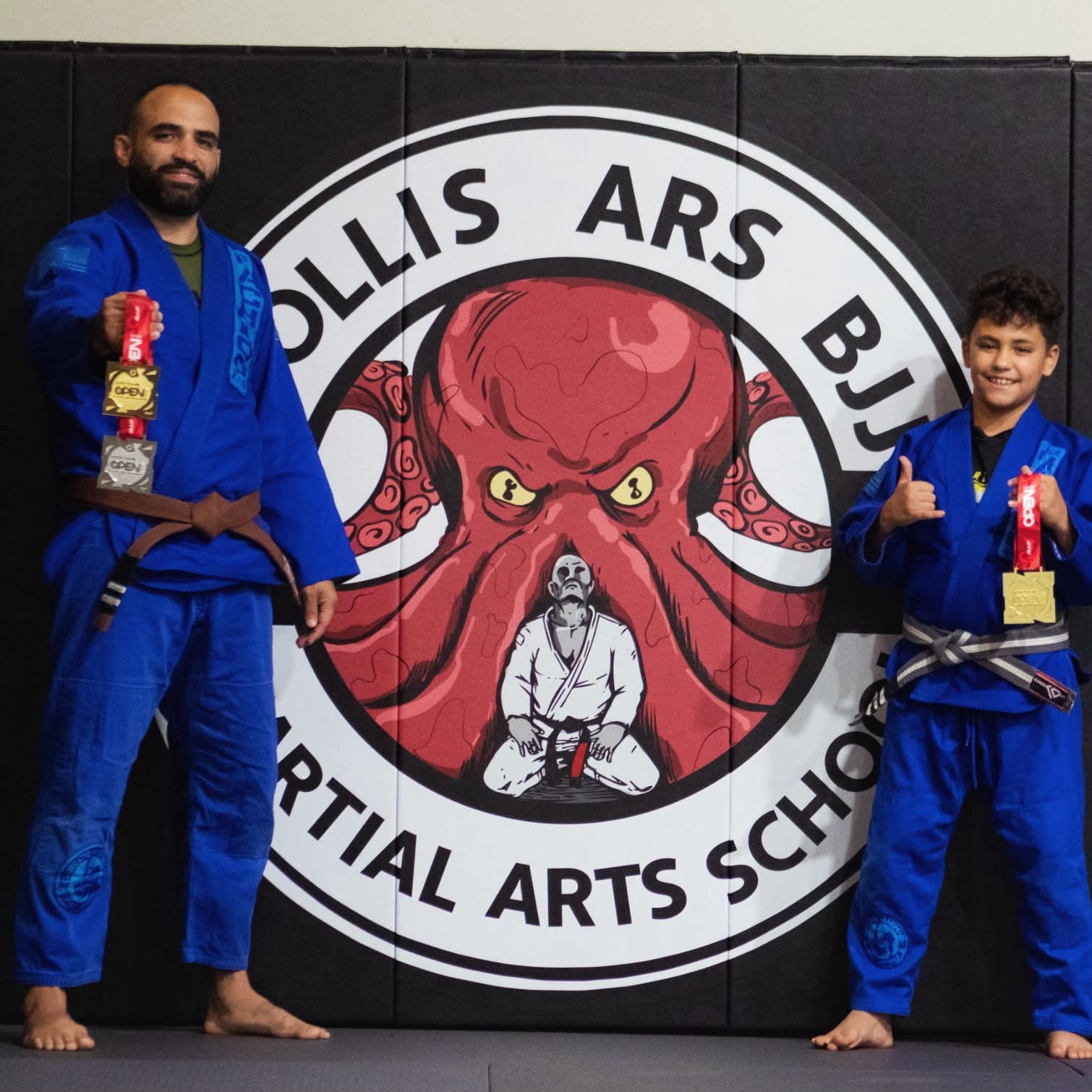 A Mollis Ars BJJ student and coach holding competition medals in front of the academy logo