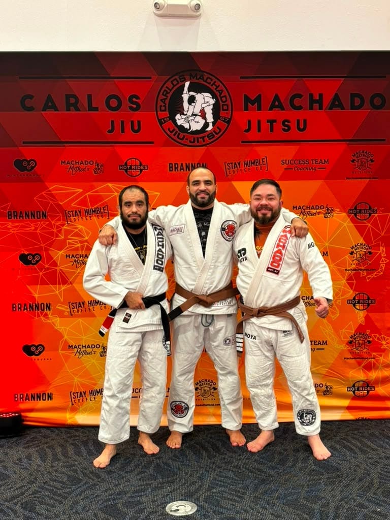 Three brown belts in front of a Carlos Machado backdrop