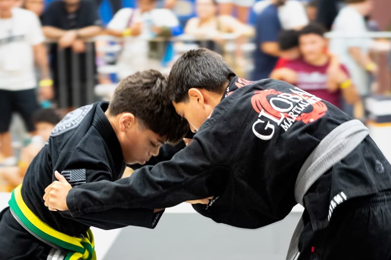 Two teenage competitors in black gis lock up head-to-head fighting for grips at a tournament.