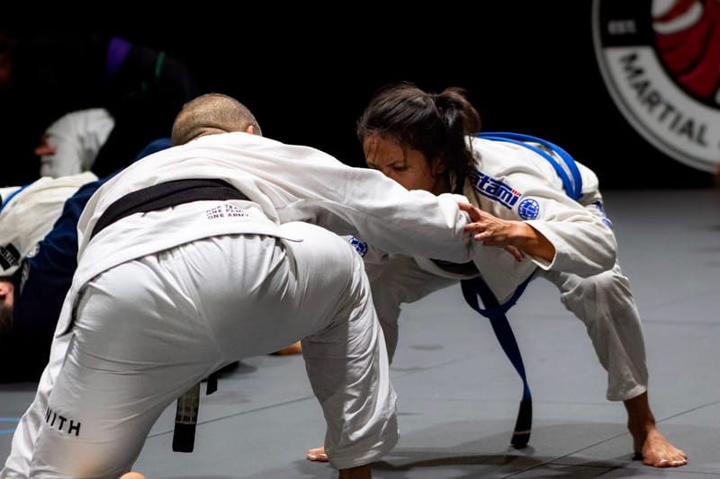 A woman in a standing grip battle with a black belt